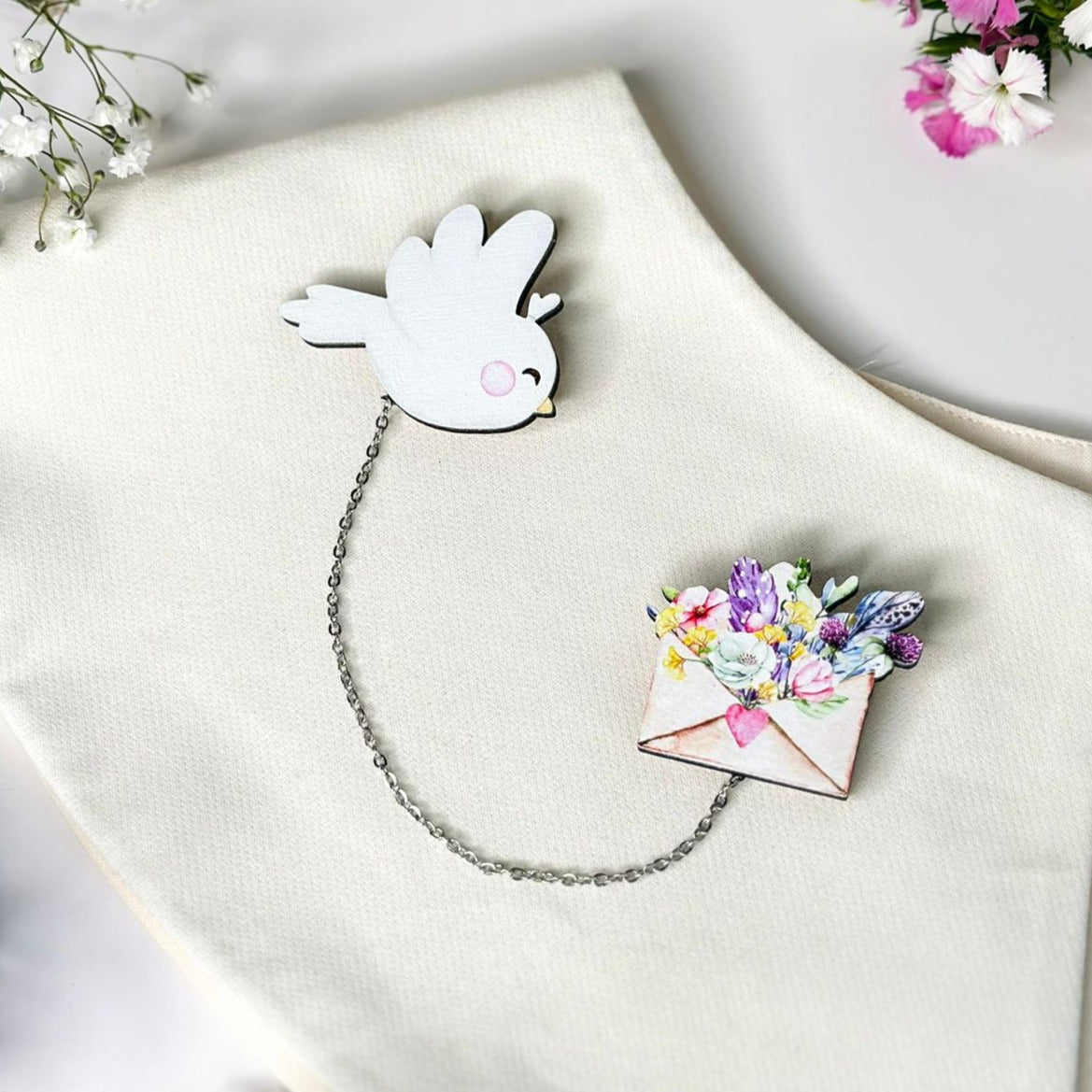 A combination of a white bird and an envelope filled with flowers, a brooch